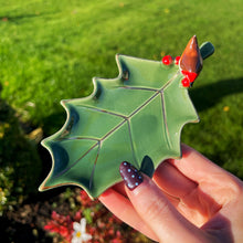 Green leaf-shaped ornament held by a hand with a blurred green outdoor background