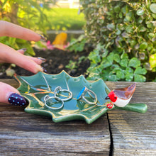 Green leaf-shaped jewelry dish with rings on a wooden surface outdoors
