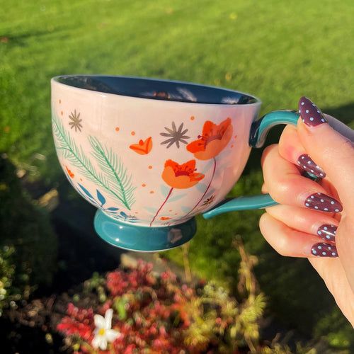 Person holding a colorful mug with floral design outdoors