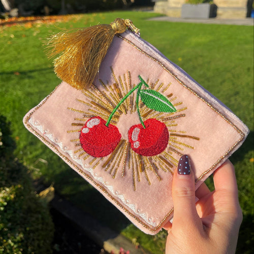 Pink pouch with cherry design held by a hand outdoors