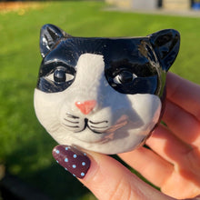 Hand holding a small ceramic cat figurine with a blurred outdoor background