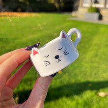 Small white cat-shaped object held by a hand outdoors on a grassy area.