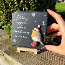 Decorative slate with a robin figurine and text, held by a hand outdoors.