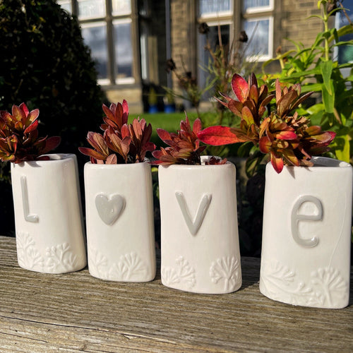 Four white ceramic pots with letters spelling 'LOVE' on a wooden surface outdoors.