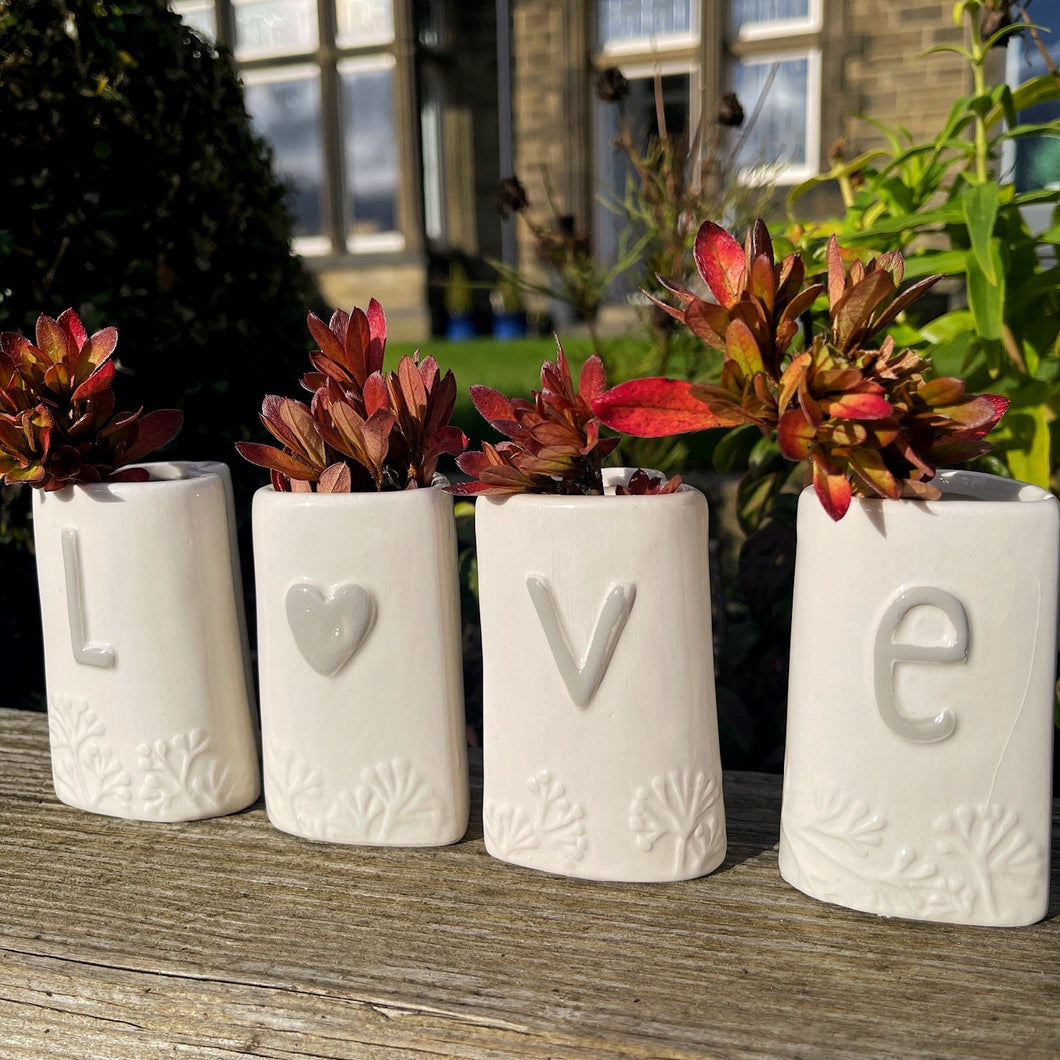 Four white ceramic pots with letters spelling 'LOVE' on a wooden surface outdoors.