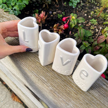 Four white ceramic pots with letters spelling 'LOVE' on a wooden surface outdoors.