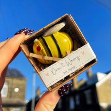 Hand holding a small box with a yellow bee-shaped object against a blue sky.