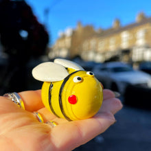 Hand holding a yellow bee-shaped object with a blurred street scene in the background