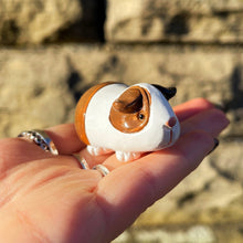 Hand holding a small guinea pig figurine against a stone wall background
