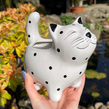 White ceramic cat-shaped object with black spots held in front of a garden background