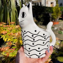 Cat-shaped mug with black patterns held in front of a garden background