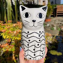 Cat-shaped ceramic mug held in a hand with a garden background