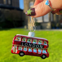 Small ornament shaped like a red London bus held by a hand outdoors.