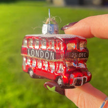 Hand holding a small red London bus ornament with a blurred outdoor background