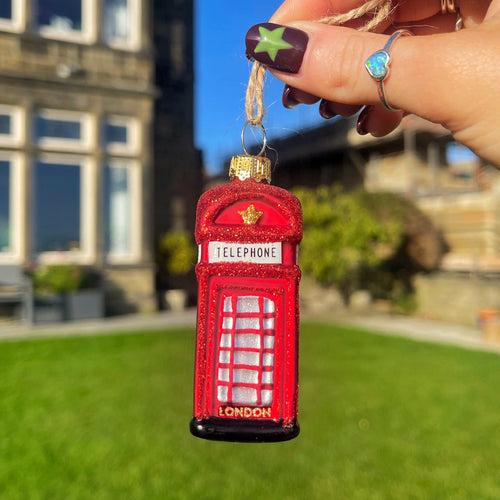 Red phone booth keychain held by a hand with a blurred outdoor background