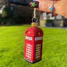Red telephone box bauble held by a hand with a blurred house and garden in the background