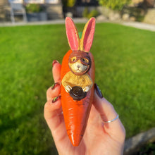 Carrot-shaped toy with rabbit design held by a hand outdoors
