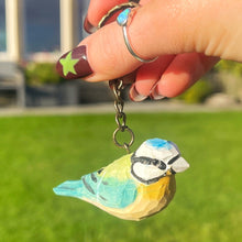 Hand holding a keychain with a bird design against a grassy background