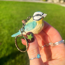 Hand holding a keychain with a bird design against a grassy background
