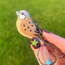 Hand holding a keychain with a bird design against a grassy background