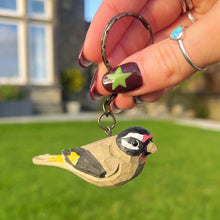 Hand holding a keychain with a bird design against a blurred outdoor background