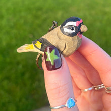 Hand holding a small bird figurine with a blurred green lawn in the background