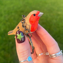 Hand holding a keychain with a red bird charm against a grassy background