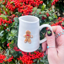 White mug with a gingerbread man design held in front of red berries