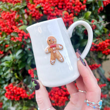 White mug with gingerbread man design held in front of red berries and green leaves