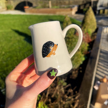 White mug with a hedgehog design held by a hand outdoors