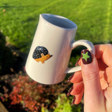 Person holding a white mug with a hedgehog design outdoors