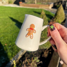 White mug with a gingerbread man design held by a hand outdoors.