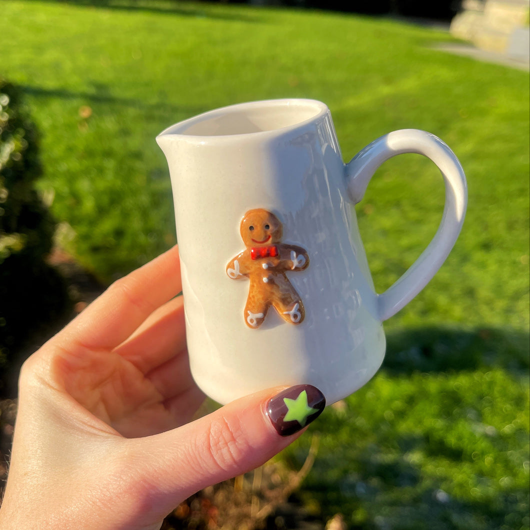White mug with a gingerbread man decoration held by a hand outdoors.