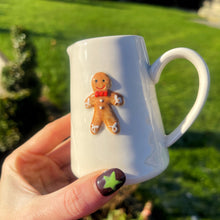 White mug with a gingerbread man decoration held by a hand against a green outdoor background