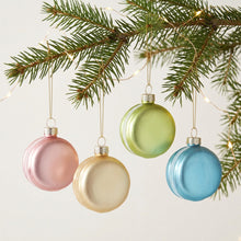 Four round hanging Christmas ornaments in pastel pink, champagne gold, light green, and sky blue, suspended by thin gold strings against a white background.